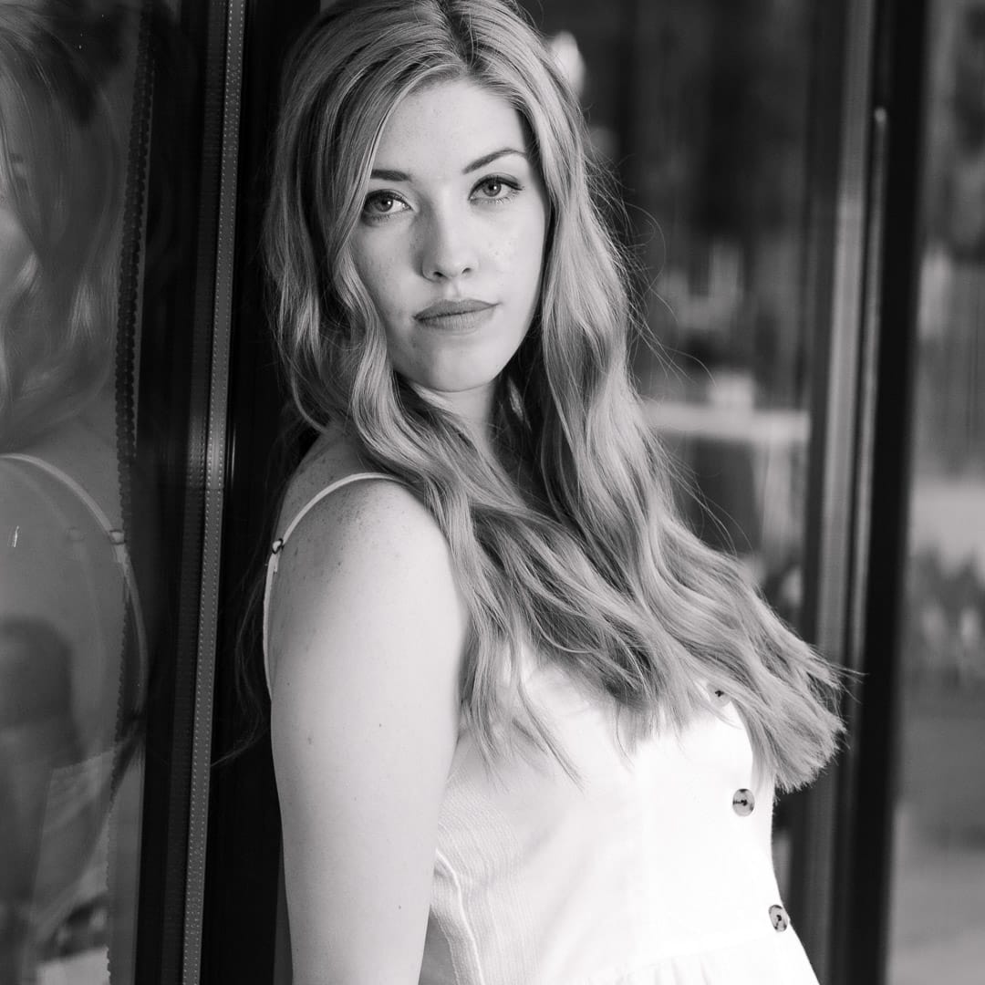 Noblesville Senior High School Student leaning against and old store window on the historic Noblesville square wearing a sleeveless white summer dress and giving off serious fashion model vibes. Credit: Studio Kate Portrait Design - Noblesville Senior Pictures