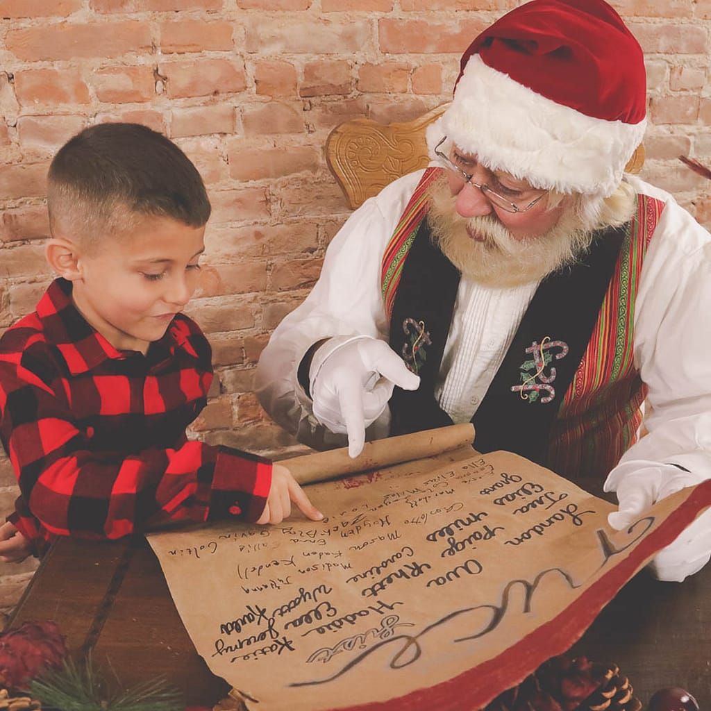 A young boy is looking through the nice list with Santa Claus as they both find it and point it out. Photographer Credit: Kate Plummer - Studio Kate Portrait Design - Noblesville Santa Experience