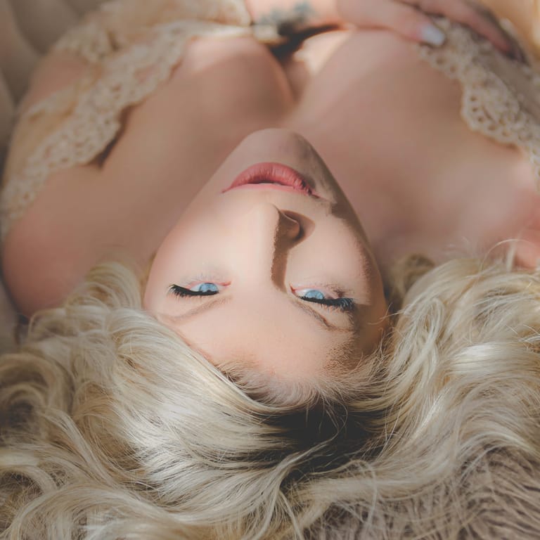This boudoir image is shot from above the blonde woman as she lays down on the couch for a break. The sunlight falls gently on her face and lace covered chest. Photo by Kate Plummer of Studio Kate Portrait Design in Noblesville, IN